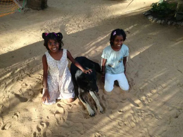 Man sieht Achini und Sachini gemeinsam mit unserem Hund im Sand sitzend.