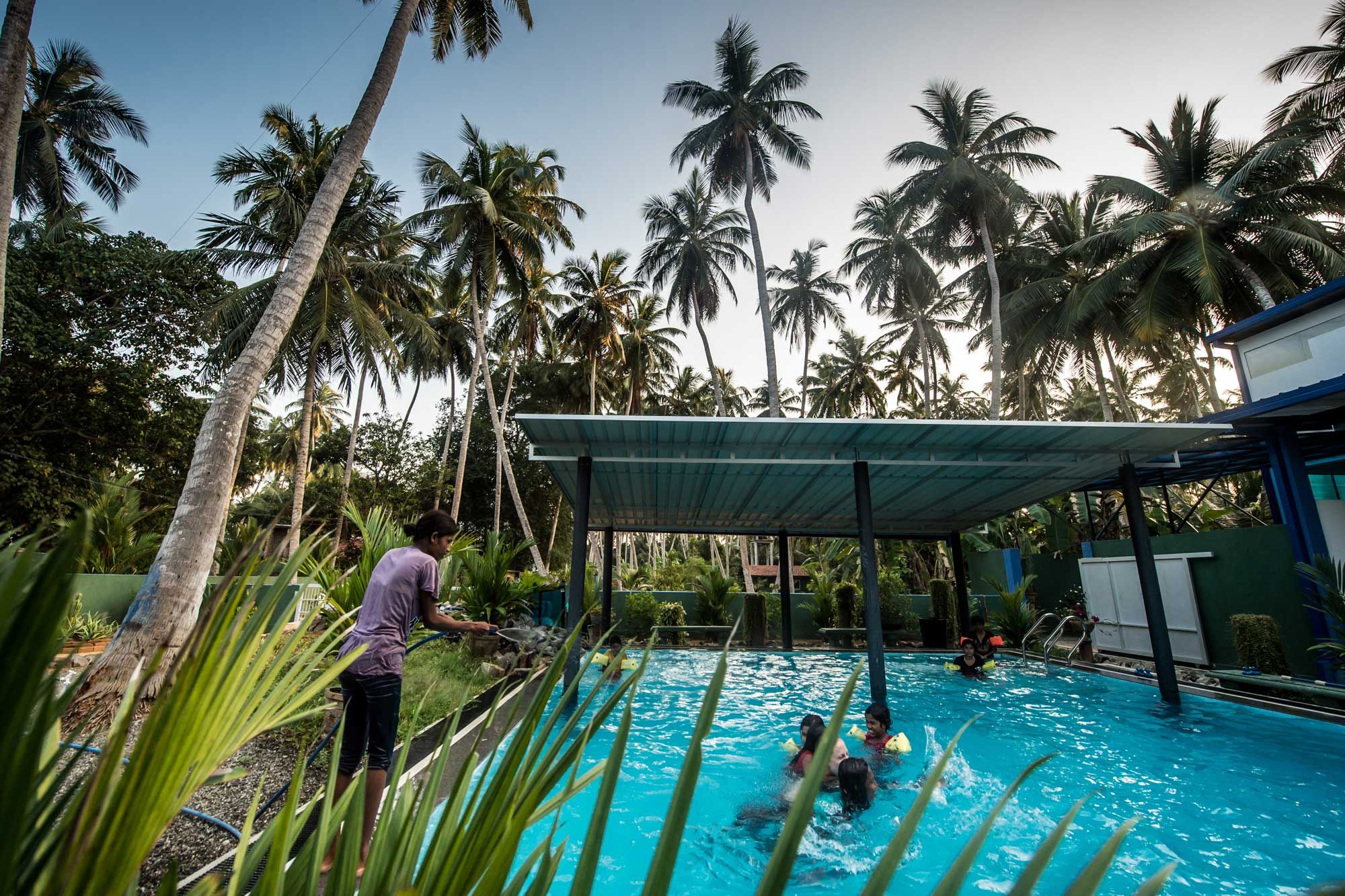 Kinder beim Schwimmen im Pool des Angels Home, umgeben von Palmen in Sri Lanka